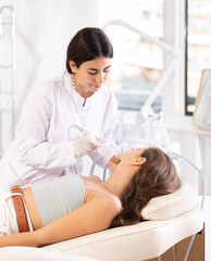 Brunette female doctor making facial beauty procedure with leather knife attachment to female patient