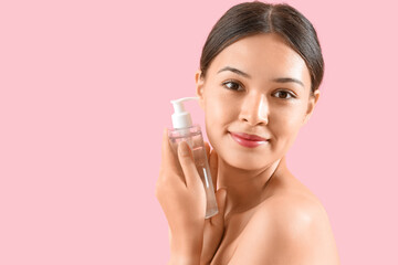 Young Asian woman with bottle of micellar water on pink background, closeup