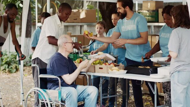 Charity organization shows devotion to fighting hunger and poverty by giving away free meals to homeless people. Warm food is provided by volunteers to caucasian wheelchair user and less privileged.