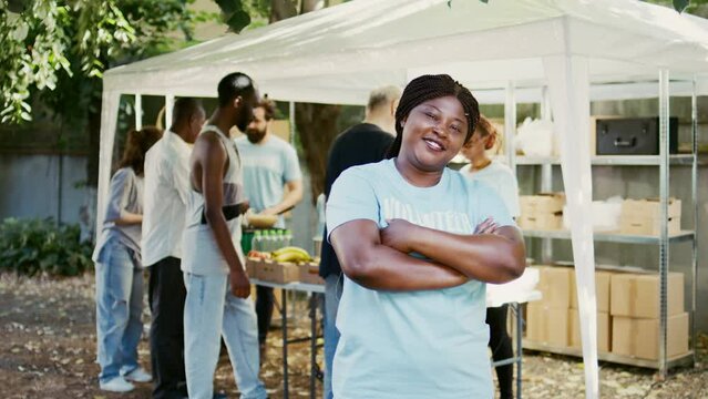 African American female volunteer grins and poses during a food drive charitable event. Humanitarian aid program that provides hunger relief and help to the homeless and the poor. Portrait shot.