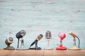 Retro old microphones for press conference or interview on table front textured light blue wooden wall background. Vintage old style filtered photo