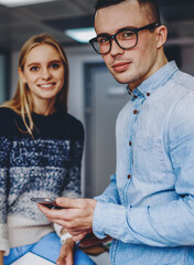 Two hipster students standing in coworking space.Young man with cellular in hand
