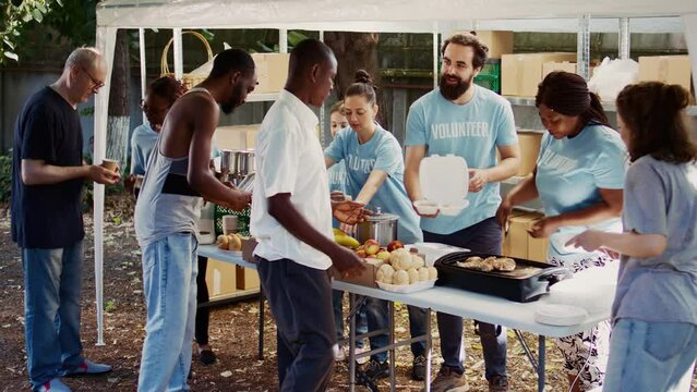 Young volunteers from Caucasian and African American communities give the less fortunate free food and necessities. Voluntary people offering humanitarian aid and hunger relief to the needy. Handheld.