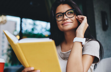 positive hipster girl in spectacles for vision correction looking away enjoy interesting book