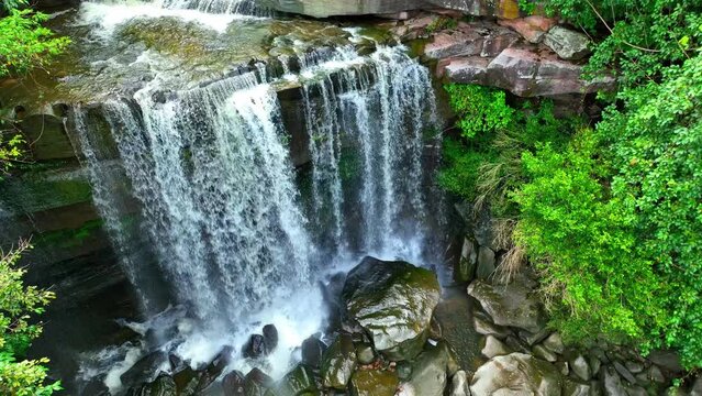 Breathtaking drone view of a majestic tropical waterfall cascading from a towering cliff in a lush forest. Thung Na Muang Waterfall, Pha Taem National Park, Ubon Ratchathani Province, Thailand.

