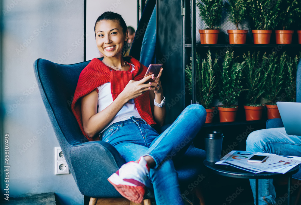 Poster portrait of cheerful cinese hipster blogger smiling at camera while chatting in social networks on s