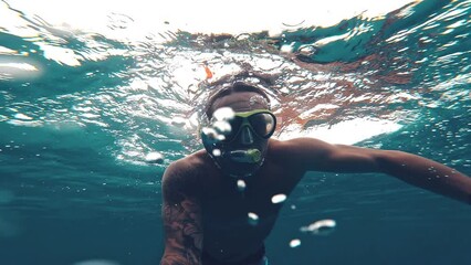 One young beautiful active man swimming and enjoying vacations outdoor in the sea snorkeling looking for fished and coral. Male person traveling holding camera having fun in the blue ocean

