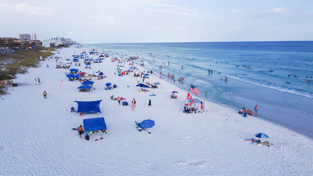 Miramar Beach white sandy shoreline, turquoise water, crowded of people swimming, relaxing, colorful tents, canopy and high-rise condo hotel buildings background, Destin, Florida