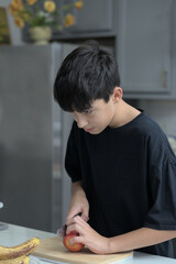 A cutting an apple using a knife without looking on the kitchen counter wearing a black t-shirt.