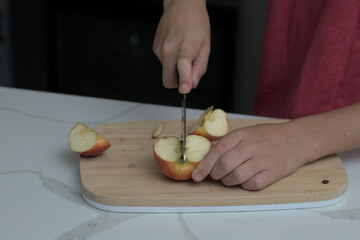 Boy hands cutting an apple with a knife on a cutting board.