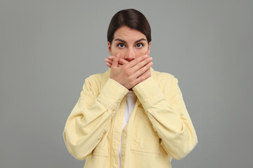 Embarrassed woman covering mouth with hands on grey background