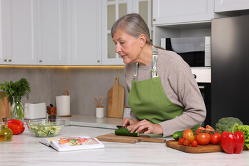 Obraz na płótnie Canvas Senior woman cooking by recipe book in kitchen