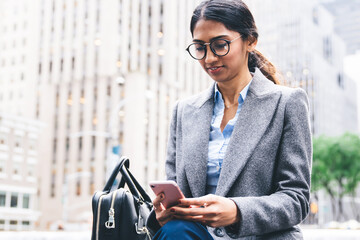 Intelligent ethnic businesswoman surfing cellphone in downtown