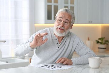 Senior man solving crossword at table in kitchen