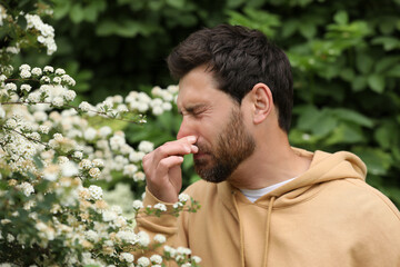 Man suffering from seasonal pollen allergy near blossoming tree on spring day