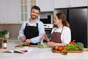 Happy couple reading recipe in culinary magazine while cooking at home