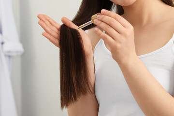 Woman applying essential oil onto hair on blurred background, closeup