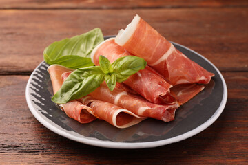 Plate with rolled slices of delicious jamon and basil on wooden table, closeup