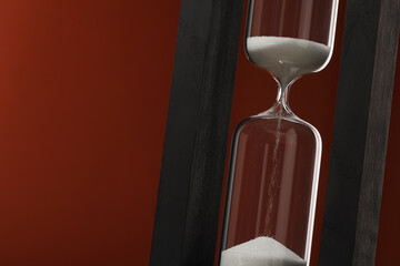 Hourglass with flowing sand on brown background, closeup. Space for text