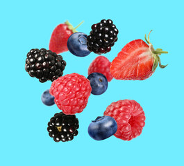 Many different fresh berries falling on light blue background