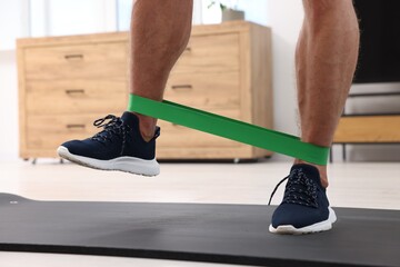 Athletic man doing exercise with elastic resistance band on mat at home, closeup