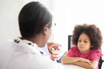 African American dentist explaining to mixed-race afro child how to brush teeth. The doctor and healthcare concept for children.