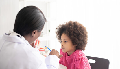 African American dentist explaining to mixed-race afro child how to brush teeth. The doctor and...