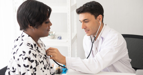 Hispanic physician check-up African American patient with stethoscope at the hospital. Healthcare medical diagnosis and examining on the laptop. Copy space background.