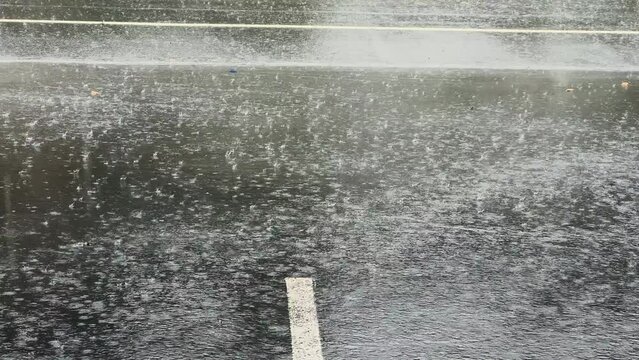 Slow Motion, heavy rain water drops falling into big puddle on asphalt, flooding the street.