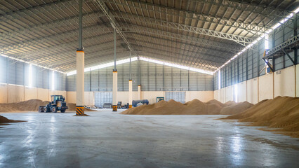Bulldozer pushing pile of dried paddy rice inside a huge bulk storage warehouse. Rice mill plant. - obrazy, fototapety, plakaty
