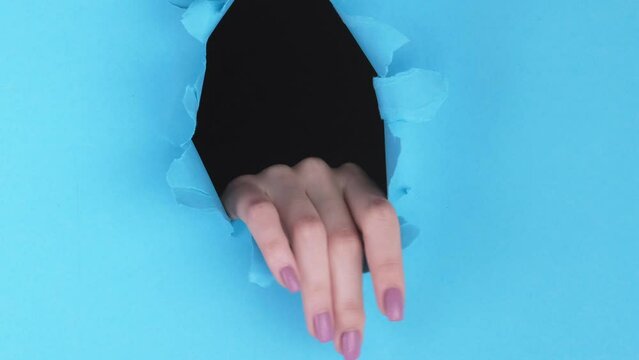 Vertical video. Breakthrough hand. Spy discovery. Gentle female fingers inside blue torn wall paper hole touching rough edge advertising background with empty space.