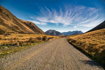 Rural gravel country road in the remote rural valley between the mountains and lakes - obrazy, fototapety, plakaty