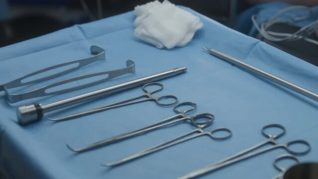 Close up shot of table with professional surgical instruments in surgery. Surgeon puts medical clip on table. Medical staff operate seriously injured patient. Medics work in modern medical facility.