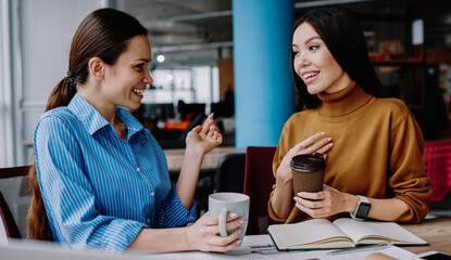 Pretty caucasian female employees having fun communicating on break with coffee