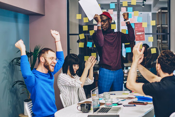 Emotional crew of multiracial employees celebrating completed project in cooperation
