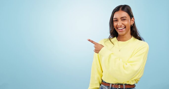 Face, hand pointing and happy woman dance in studio for promotion, announcement or deal on blue background. Portrait, smile and Indian female model excited for platform, service or sign up offer