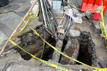 A hole in the ground with messy cable instalation in the middle of the road. Asphalt that has...