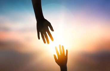 Silhouette of giving a helping hand over sunset background.