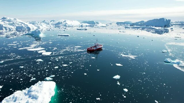 Amazing aerial view of ship sailing in Icefjord, Greenland. Polar coastal scenery of icebergs and calm ocean.