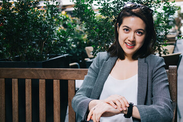 Smiling Asian woman checking watch on bench