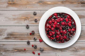Pie with berries top view, raspberry, currant, strawberry on a white plate on a wooden background, near red currant and cherry berries