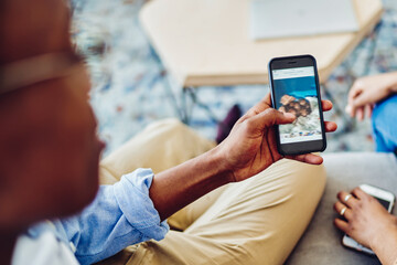 Cropped image of man using mobile phone showing content to girlfriend sitting at sofa at home interior