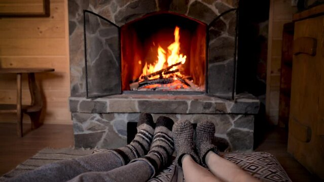 Couple in wool socks warming by cozy fire. Romantic winter evening together