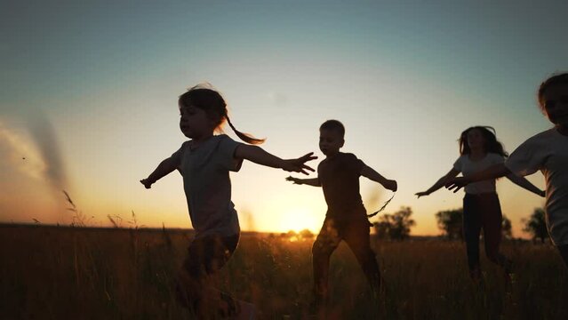 Active happy family. Group of kid run together across field at sunset.Team of kid active games in nature.Silhouette of happy children outdoors in park.Kid child run on green grass.Children family play