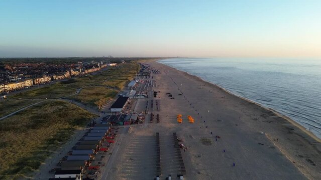Beautiful flight in summer over the beach in Katwijk aan Zee. People are resting near the sea. Houses for tourists. Beach umbrellas, rides, people swimming in the sea. Beach in Netherland. North Sea.