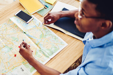 Top view of african american hipster guy pointing on destination on map planning journey vacations