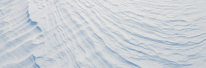 Beautiful winter background with snowy ground. Natural snow texture. Wind sculpted patterns on snow surface. Wide panoramic texture for background and design.
