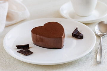 Valentine s day dessert, delicious dark chocolate mousse heart-shaped on white plate with spoon, cup of tea or coffee and napkin