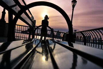 Silhouette of a Young Woman Watching the Sunset by a Bench in Battery Park - Manhattan, New York...
