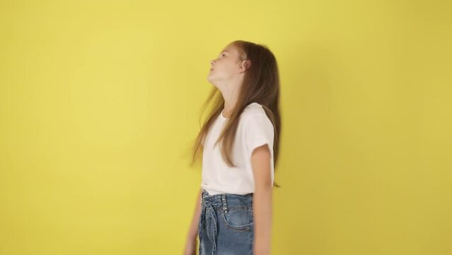 Serious cute little schoolgirl shaking head no, expessing rejection and denial, yellow studio background